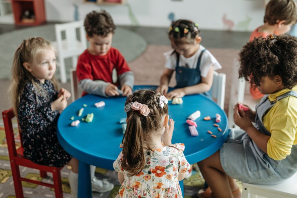 Group of preschool children sitting around a table playing with colorful modeling clay